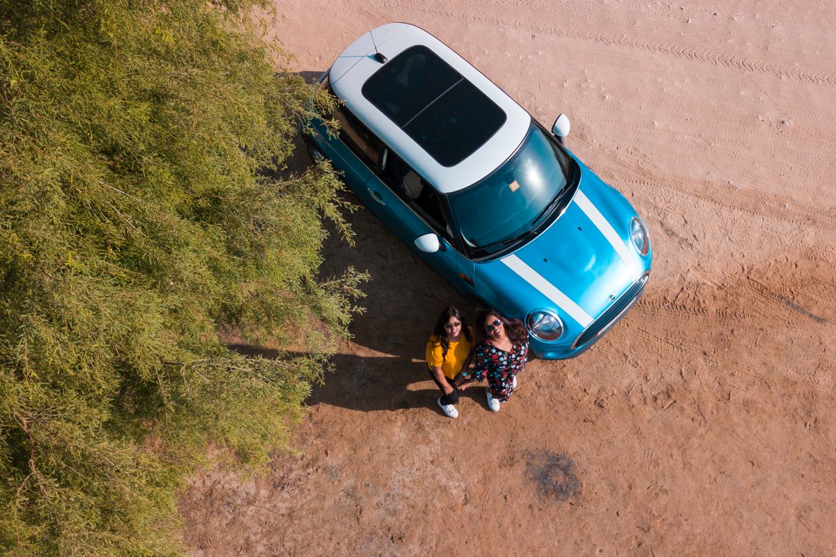Foto aérea de duas mulheres ao lado de um carro azul
